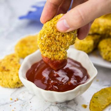 eine Hand, die ein veganes Chicken Nugget in Ketchup tunkt
