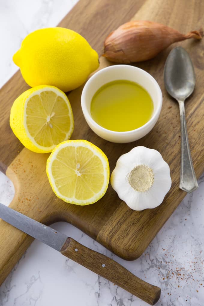 Zitronen, Olivenöl, Knoblauch und eine Schalotte auf einem Holzbrett