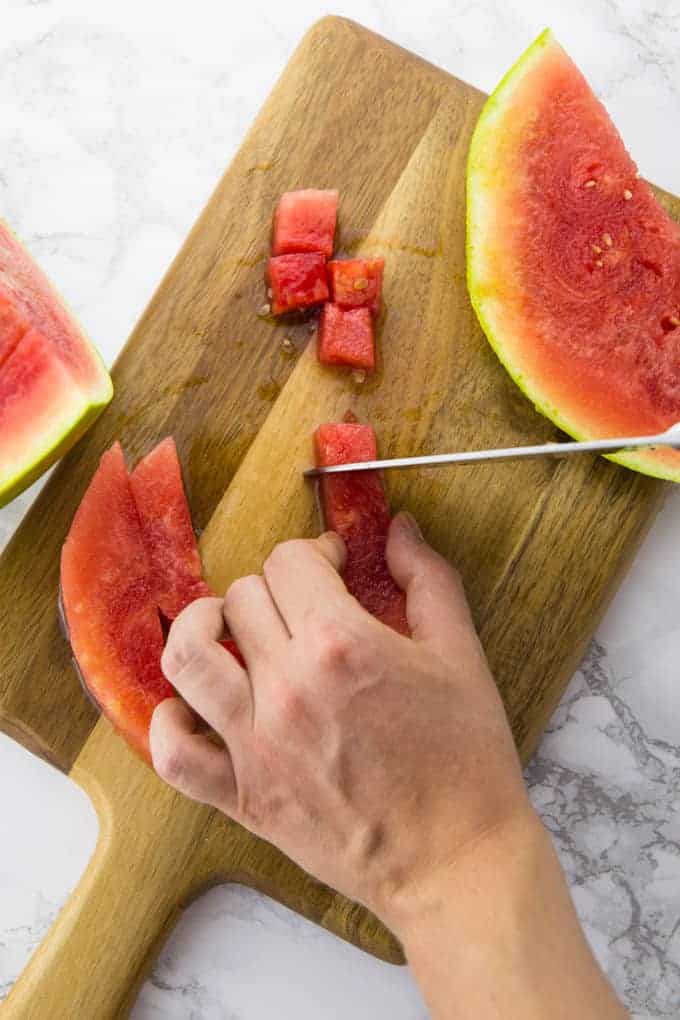 Wassermelonenscheiben werden auf einem Brettchen in Würfel geschnitten