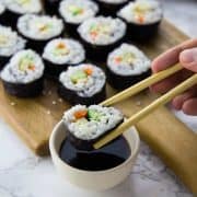 Ein Sushi wird mit Essstäbchen in Sojasauce gedopt mit mehr Sushi im Hintergrund