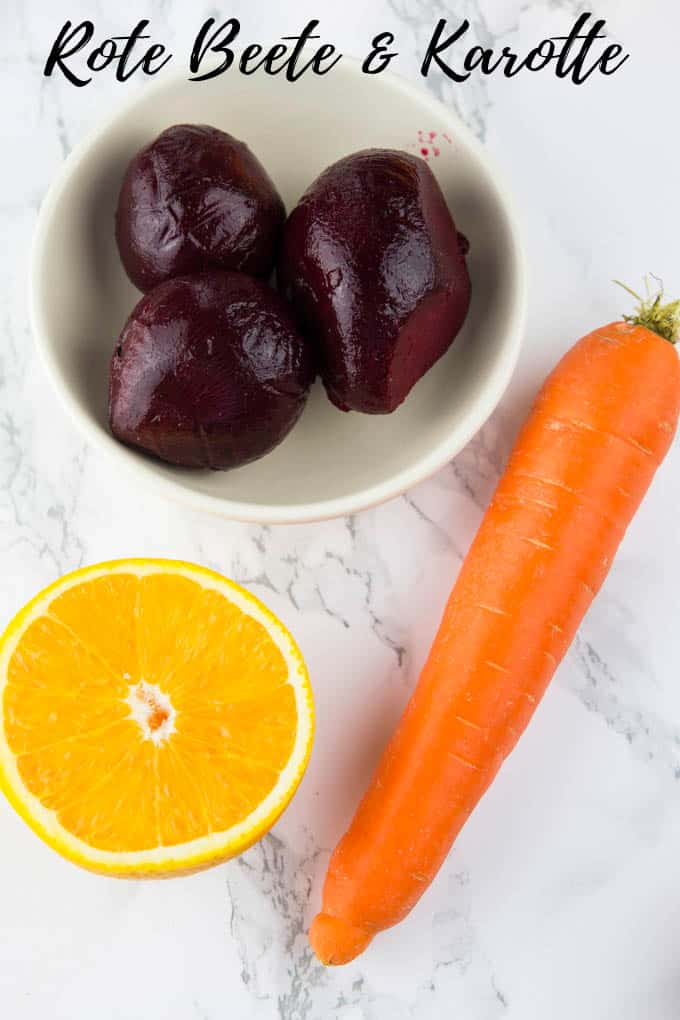 eine halbe Orange, eine Karotte sowie rote Beete in einer kleinen Schüssel auf einer Marmorarbeitsplatte mit der Aufschrift "Rote Beete & Karotte"