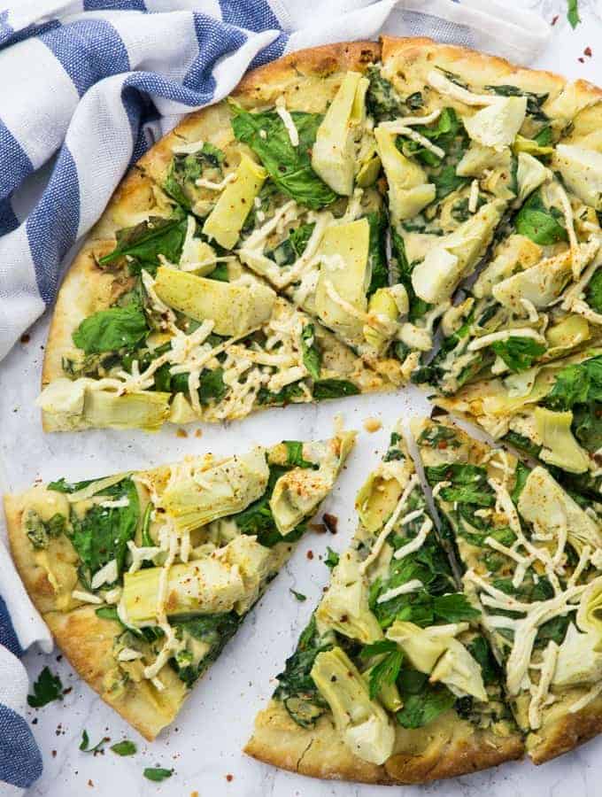 Vegane Pizza mit Artischocken und Spinat auf einer weißen Arbeitsplatte