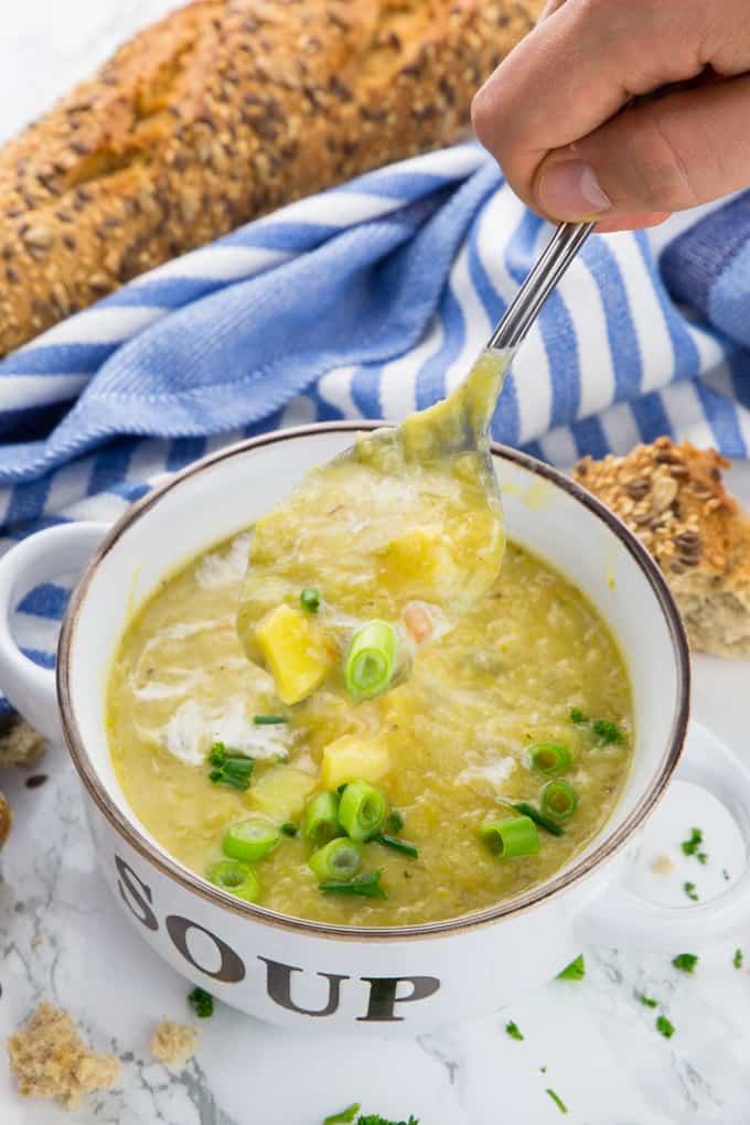 eine Suppenschüssel mit Kartoffelsuppe sowie einer Hand mit Löffel, die Suppe löffelt und Brot im Hintergrund