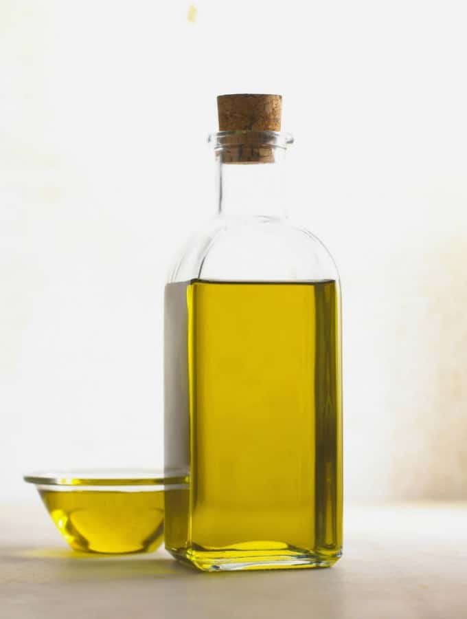 Öl in einer Glasflasche mit einem kleinen Glasschälchen mit Öl neben der Flasche 