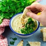 Baba Ganoush in einer blau weißen Schüssel mit einer Hand, die ein Pita Brot hinein tunkt