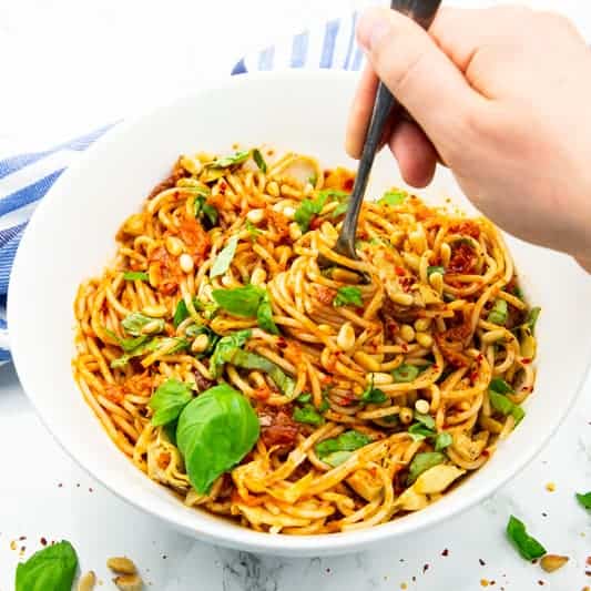Spaghettisalat in einer weißen Schüssel mit einer Hand, die mit einer Gabel Spaghetti aufrollt