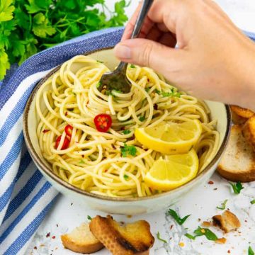 spaghetti aglio e olio in einem beigen Teller mit einer Hand, die Spaghetti mit einer Gabel aufrollt