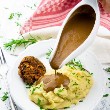 eine Hand gießt vegane Bratensoße aus einer Soßenschüssel über einen Teller mit Kartoffelpüree