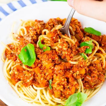 ein Teller mit Spaghetti Bolognese mit einer Hand, die eine Gabel hält