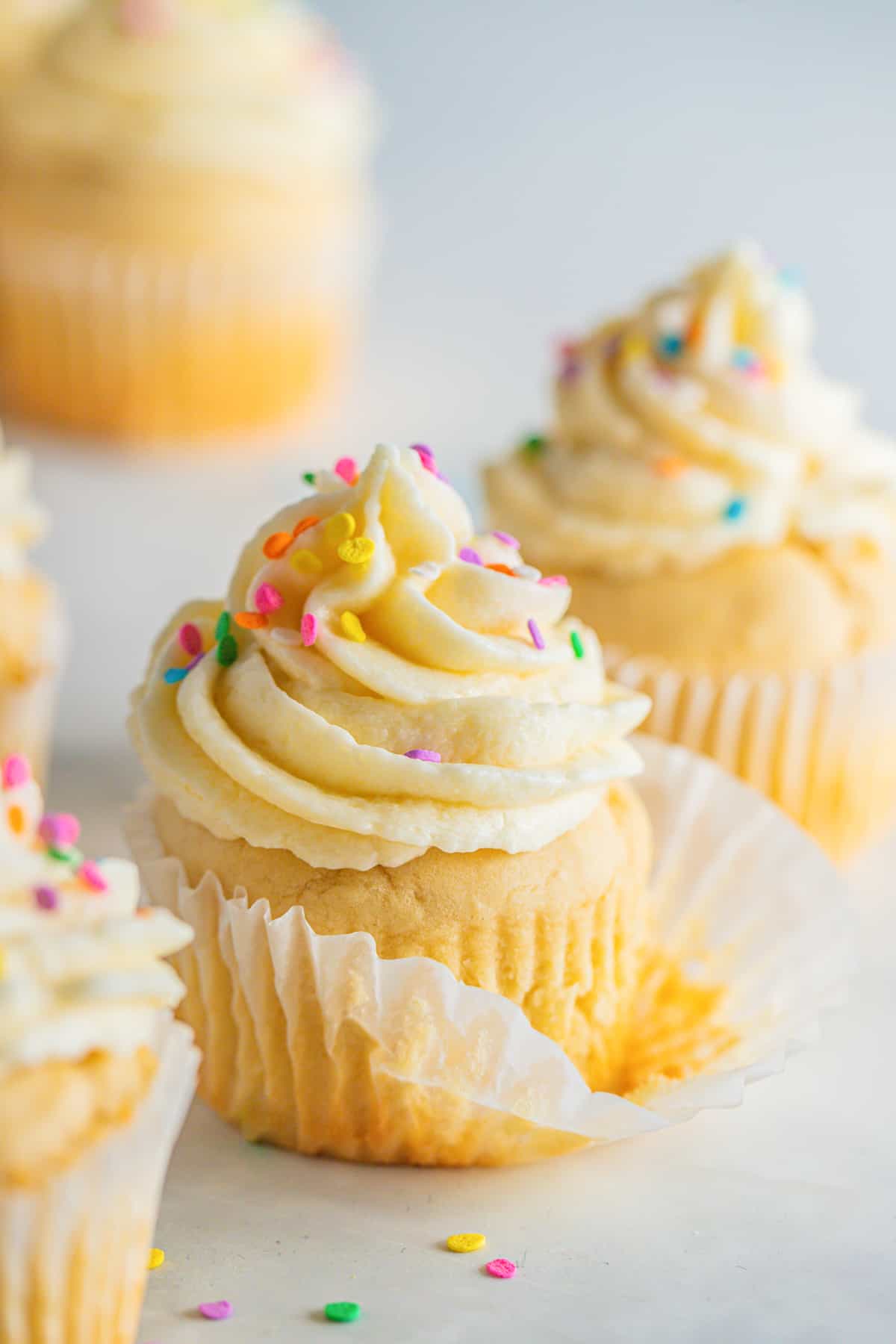 ein Cupcake mit Vanille Frosting in einem Papierförmchen mit mehr Cupcakes im Hintergrund 