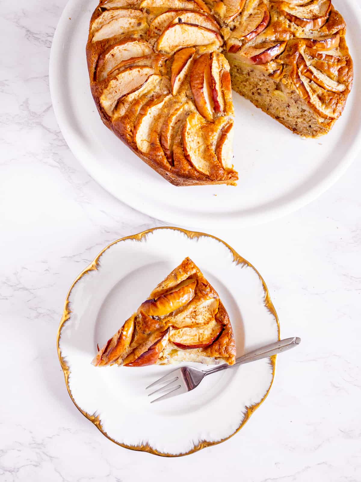 ein Stück veganer Apfelkuchen auf einem weißen Teller mit dem restlichen Kuchen im Hintergrund 