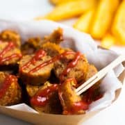 Vegane Wurst aus Seitan in Scheiben mit Ketchup in einer Papierschale mit Pommes im Hintergrund