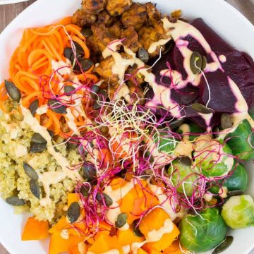 Buddha Bowl mit Quinoa, Kürbis und Tempeh in einer weißen Schüssel auf einem Holzbrett