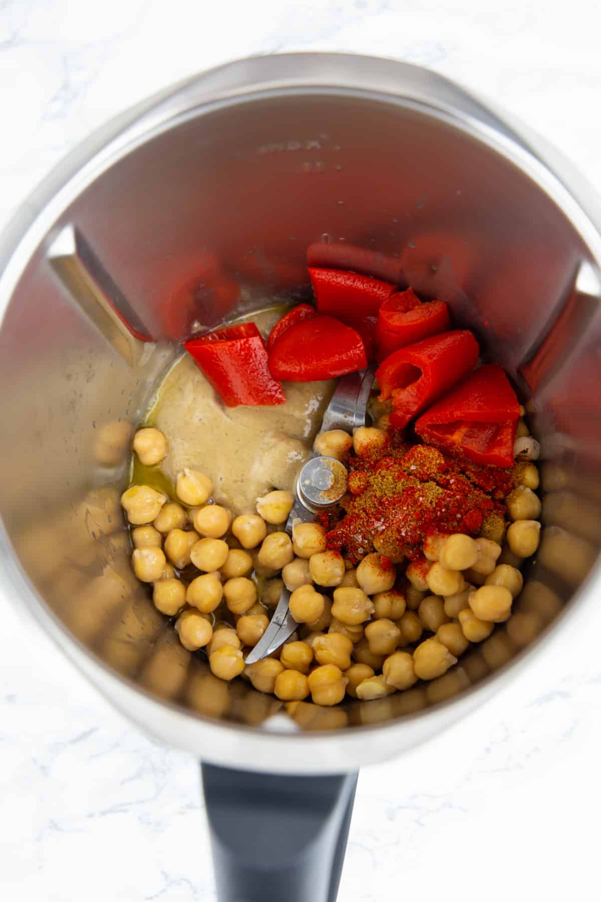 die Zutaten für Paprika Hummus in einem Mixbehälter auf einer Marmorplatte