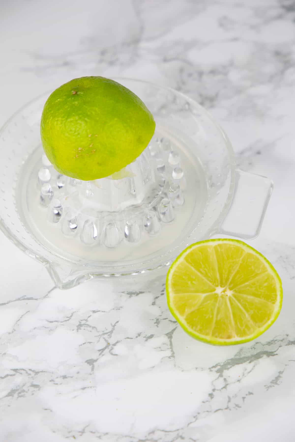 eine Zitronenpresse auf Glas auf einer Marmorplatte mit zwei Limettenhälften