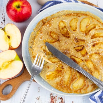 zwei Apfelpfannkuchen auf einem Teller mit Besteck und frischen Äpfeln Nebendran