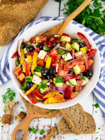 Griechischer Salat in einer weißen Schüssel mit Brot im Hintergrund