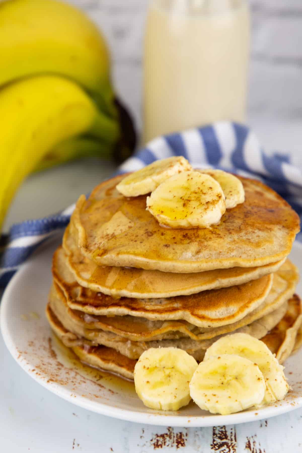 Bananen Pancakes mit Bananenscheiben auf einem weißen Teller mit einer Flasche Milch im Hintergrund