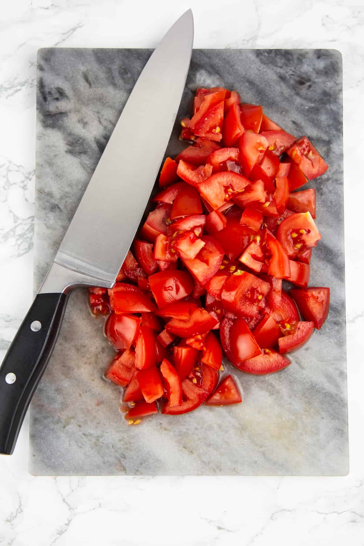 gewürfelte Tomaten auf einem Marmorschneidebrett mit einem großen Messer daneben 