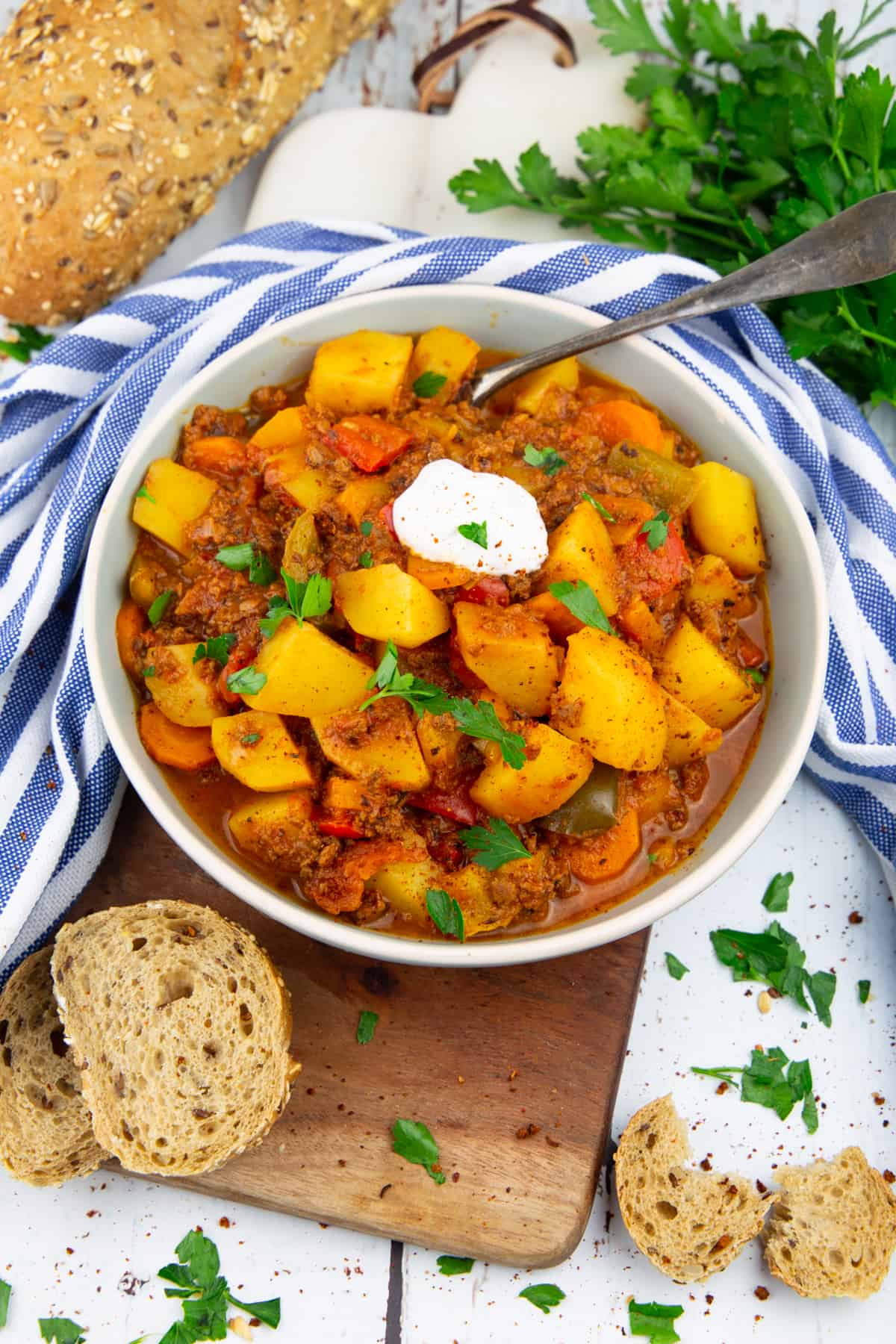 ein Teller mit einem Kartoffeleintopf mit Paprika auf einem Holzbrett 