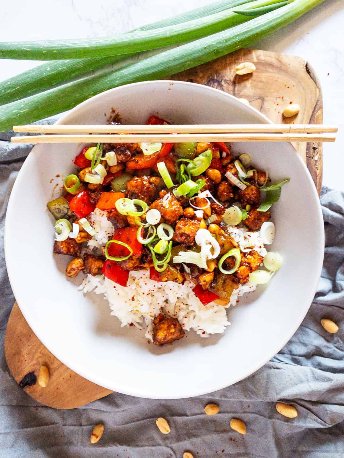 Kung Pao Tofu mit weißem Reis und Erdnüssen in einem weißen Teller auf einem Holzbrett 