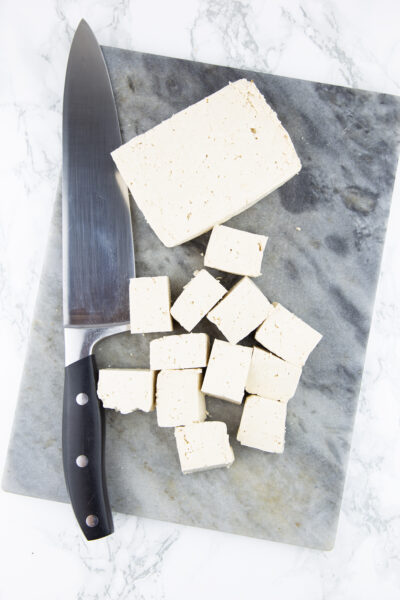 Tofu in Würfel auf einem Marmorschneidebrett mit einem Messer auf der Seite