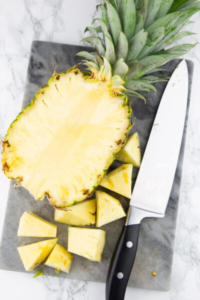 eine halbierte Ananas auf einem Schneidebrett mit einem Küchenmesser daneben