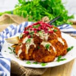 Gebackener Blumenkohl mit Tahinisauce, Petersilie und Granatapfel auf einem weißen Teller auf einem Holzbrett