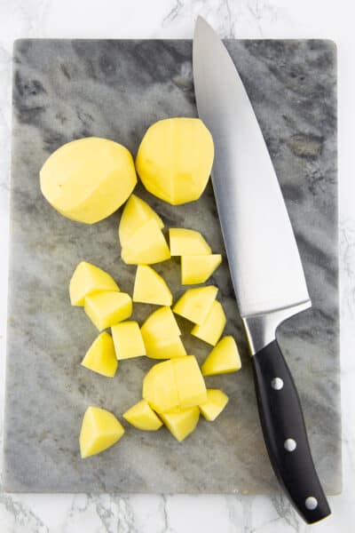 gewürfelte Kartoffeln auf einem Schneidebrett mit einem großen Messer
