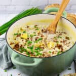 ein grüner Topf mit Hack Lauch Suppe auf einem weißen Holzbrett mit Brot und Schnittlauch im Hintergrund