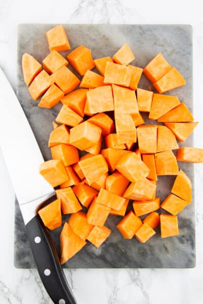Süßkartoffelwürfel auf einem Marmorschneidebrett mit einem Messer daneben 