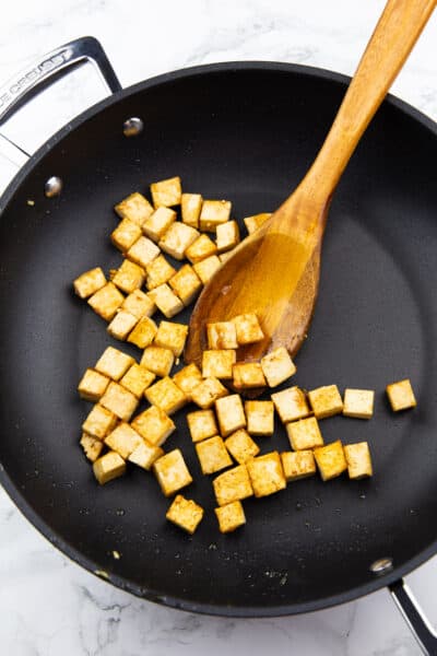 Tofuwürfel in einer schwarzen Pfanne mit einem Kochlöffel 