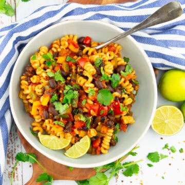 ein grauer Teller mit Nudeln mit Paprika und schwarzen Bohnen auf einem Holzbrett mit frischem Koriander neben dem Teller