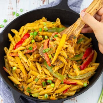 eine schwarze Pfanne mit Pasta Rasta mit einer Hand, die einen Holzlöffel mit Pasta hochhält