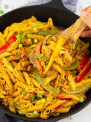 eine schwarze Pfanne mit Pasta Rasta mit einer Hand, die einen Holzlöffel mit Pasta hochhält