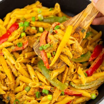 eine schwarze Pfanne mit Pasta Rasta mit einer Hand, die einen Holzlöffel mit Pasta hochhält