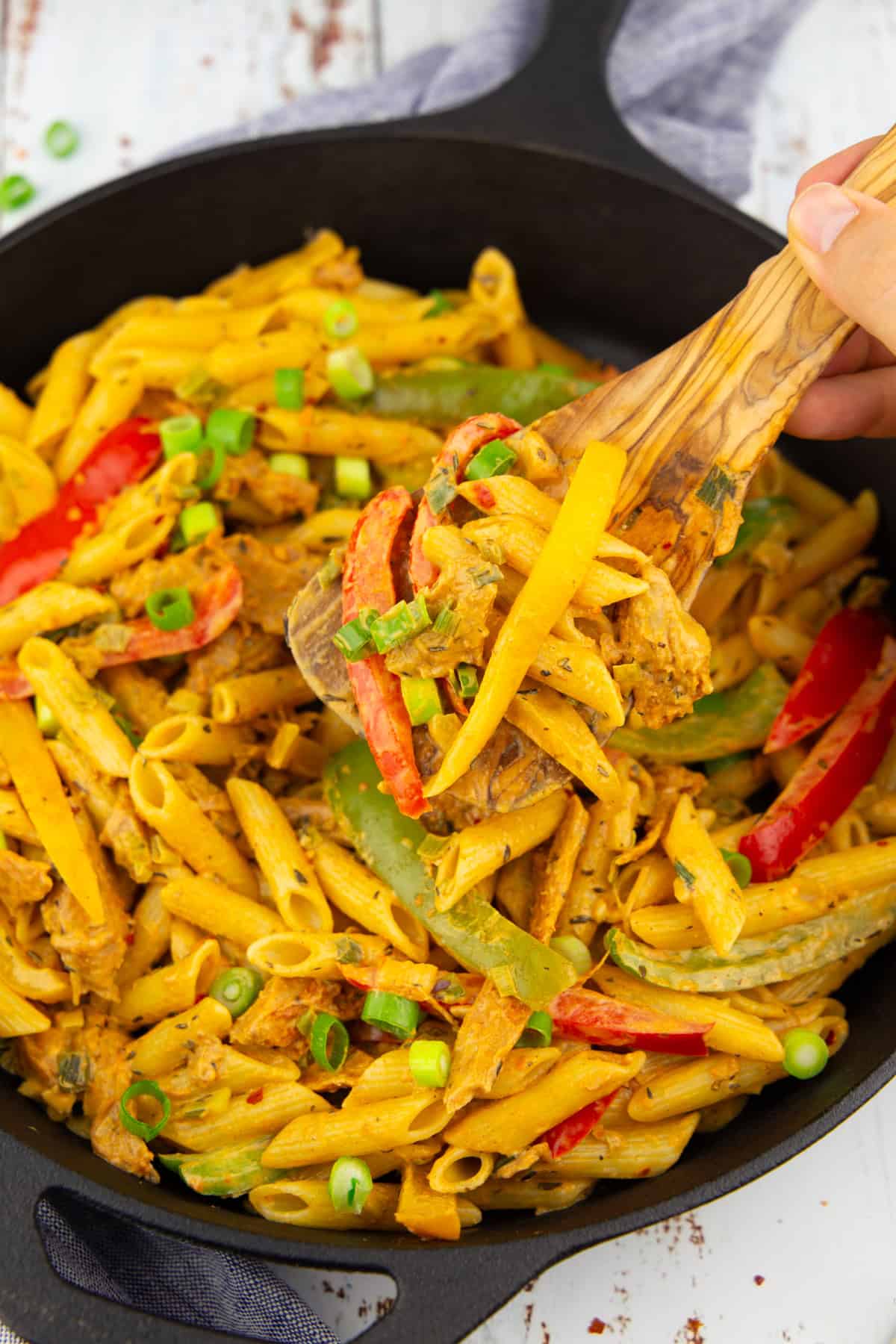 eine schwarze Pfanne mit Pasta Rasta mit einer Hand, die einen Holzlöffel mit Pasta hochhält