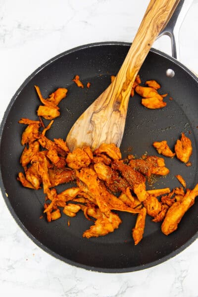 eine Pfanne mit knusprig angebratenen veganen Hähnchenstreifen mit einem Holzlöffel