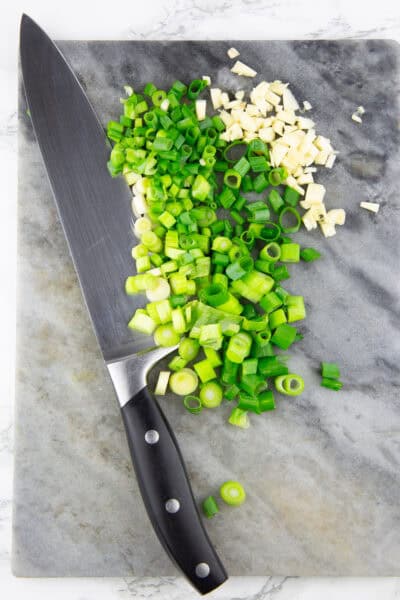 ein Marmorschneidebrett mit einem Messer und zerkleinerten Frühlingszwiebeln und Knoblauch