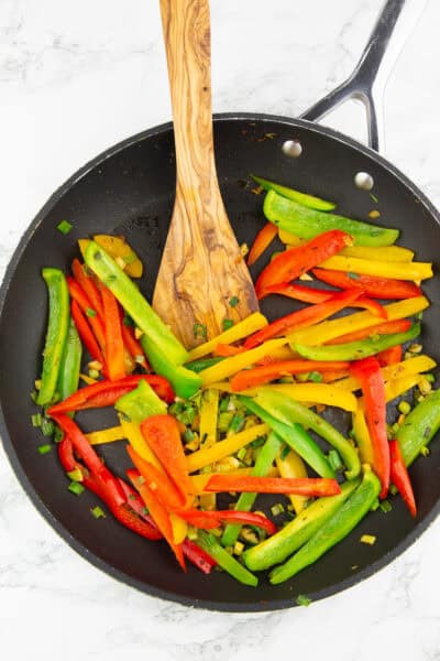eine schwarze Pfanne mit Paprikastreifen mit einem Holzlöffel