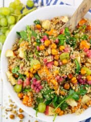 eine weiße Schüssel mit Quinoa Salat mit Süßkartoffeln auf einem weißen Holzbrett