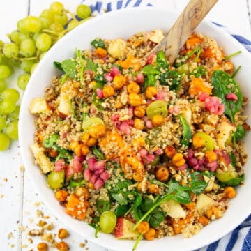 eine weiße Schüssel mit Quinoa Salat mit Süßkartoffeln auf einem weißen Holzbrett