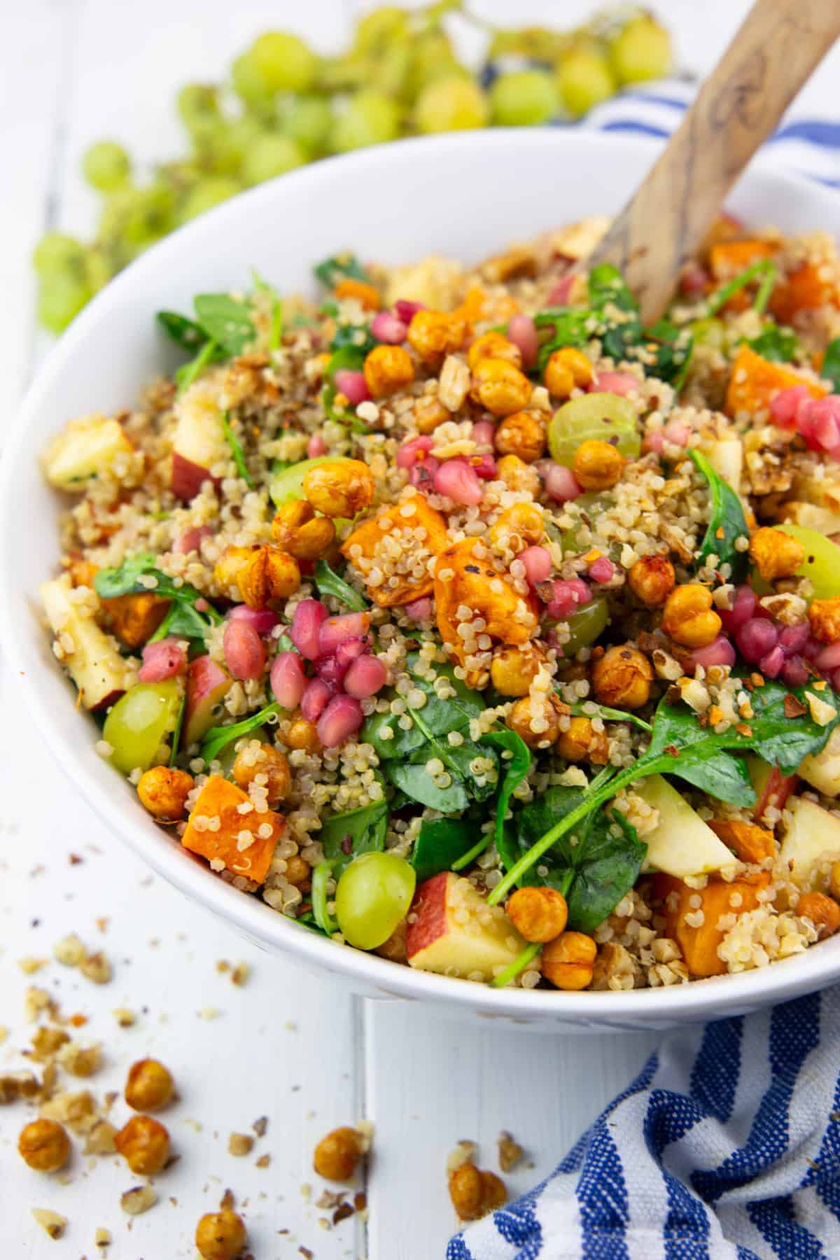 eine weiße Schüssel mit einem herbstlichen Quinoa Salat mit Süßkartoffel, Spinat und Trauben auf einem weißen Holzbrett